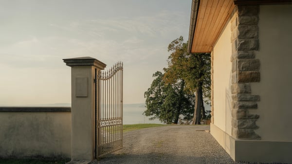 Halb geöffnetes Gartentor in einer Steinmauer vor einer Villa am See
